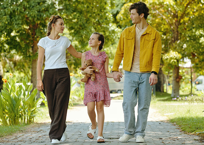 Pareja caminando con su hija en el parque, capturando el tiempo en familia con niños en casa, tomando de la mano y llevando un oso de peluche.