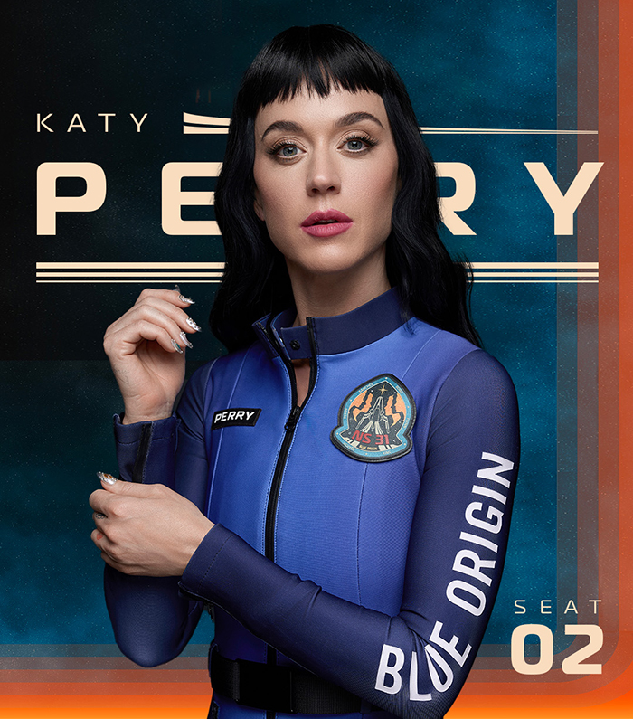 Katy Perry en un traje espacial de origen azul, de pie con confianza con los brazos doblados y con una insignia de misión.