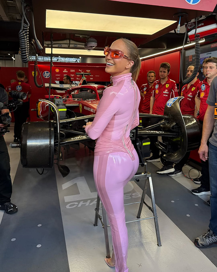 Persona en rosa Catsuit en Saudi F1 Race, de pie junto a un automóvil en el área de garaje, rodeada de miembros del equipo.