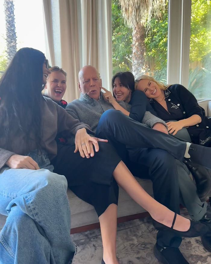 Grupo sentado en un sofá, sonriendo, con luz solar a través de las ventanas; Bruce Willis con amigos y familiares en medio del viaje de demencia.