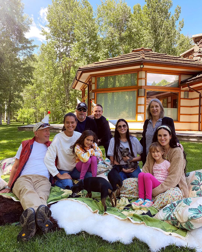 La reunión familiar en un césped, incluida la esposa de Bruce Willis, una casa en el fondo y perros que juegan cerca.
