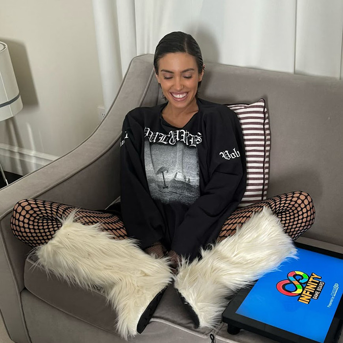 Mujer sentada en el sofá en una pose relajada con botas peludas, sonriendo, teléfono cercano.