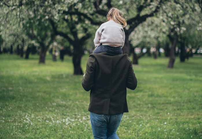 Los padres que llevan a los niños sobre los hombros a través del Parque Green durante la primavera.