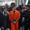 Luigi Mangione, con un mono naranja brillante, está rodeado de oficiales de la policía de Nueva York, incluidos algunos con armas.