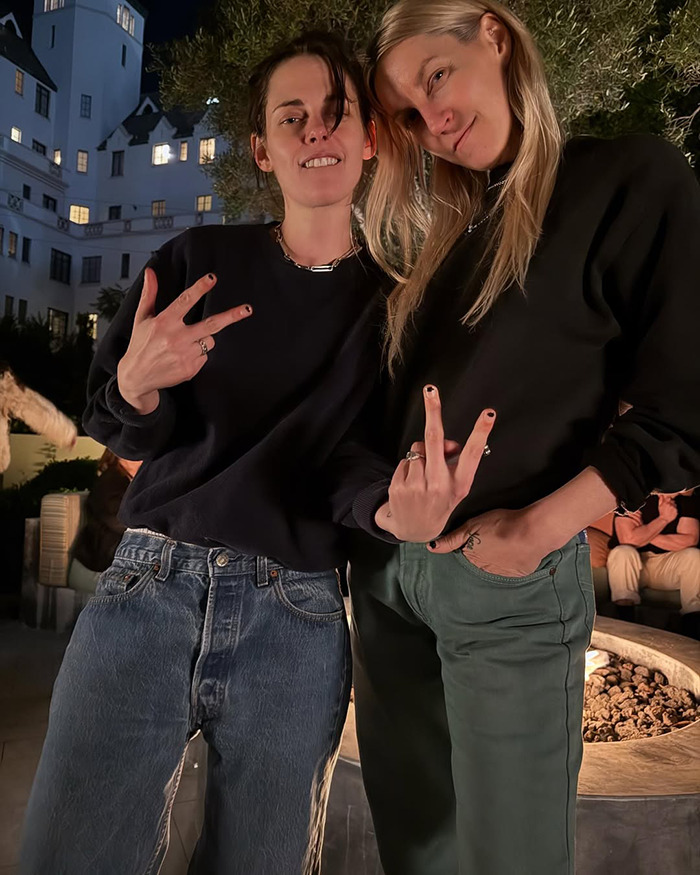 Los tortolitos Kristen Stewart y Dylan Meyer posan juntos al aire libre, mostrando señales de paz con atuendos casuales.