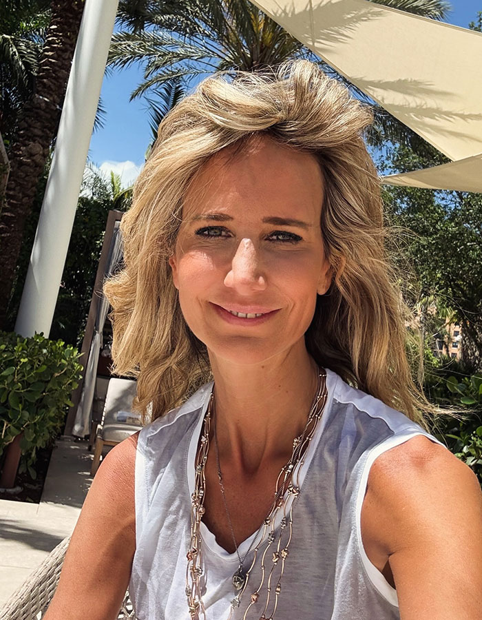 Mujer con una tapa y collar sin mangas blancas, sonriendo al aire libre bajo una sombrera, relevante para el Príncipe Andrew News.