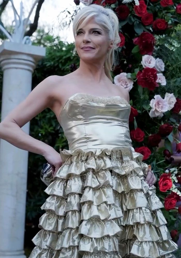 Selma Blair en la alfombra roja, con un vestido dorado con volantes, mostrando su increíble personalidad en medio del fondo floral.