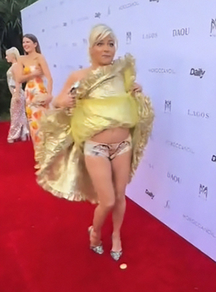 Selma Blair mostrando personalidad en un atuendo dorado y bragas con temática de gatitos en la alfombra roja.