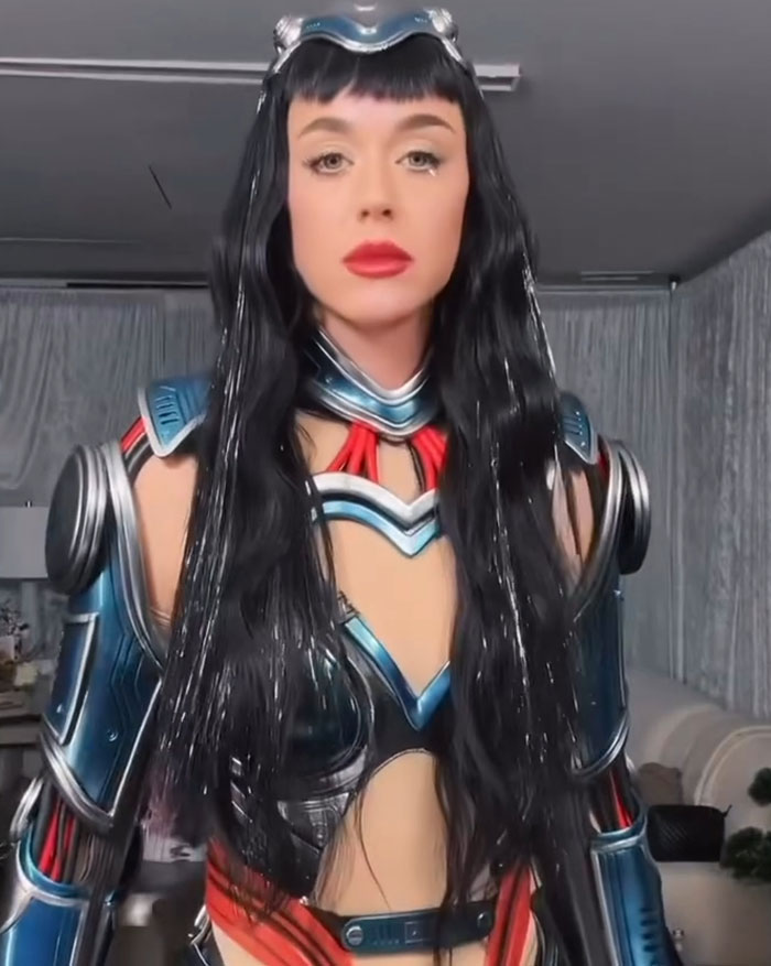 Katy Perry con disfraz de armadura futurista con cabello negro largo, dirigiéndose a los críticos de su vuelo espacial de origen azul.