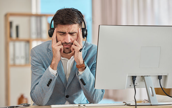 Hombre frustrado con auriculares en la computadora, frente al problema de escalada del cliente en el trabajo.