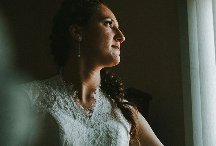 Bride in Wedding Dress mirando por la ventana, expresando preocupación por los cambios en la lista de invitados a la boda.