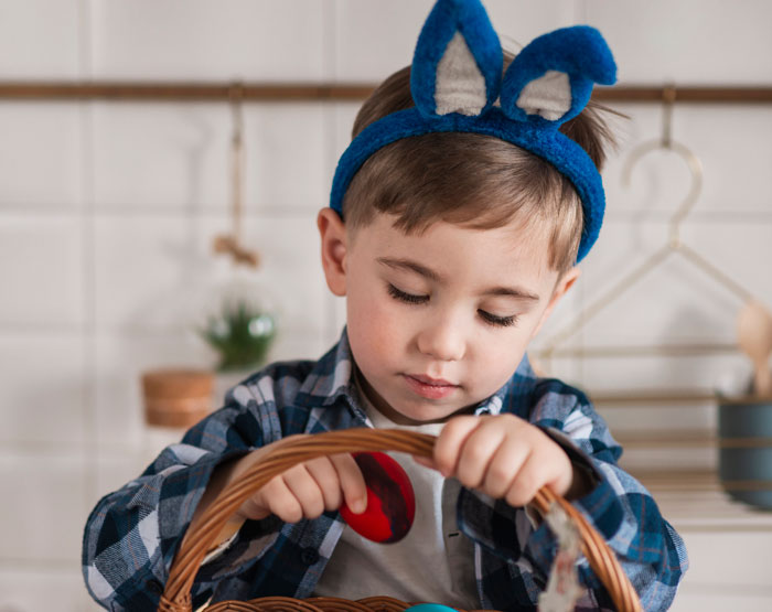 Niño con orejas de conejito explora una canasta de Pascua.