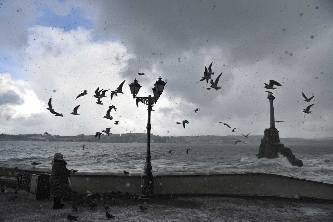 Una mujer mira a las gaviotas volando sobre el monumento a los barcos escurlidos, derecha, durante un clima de tormenta en Sevastopol, Crimea, el 13 de febrero de 2021. El monumento marca el escurador de los barcos rusos en 1854 para proteger el puerto de las tropas aliadas (Reino Unido, francés y el Piedmonte de Italia) que aterrizó en el crimeano y el puerto de la puerto de la puerto.