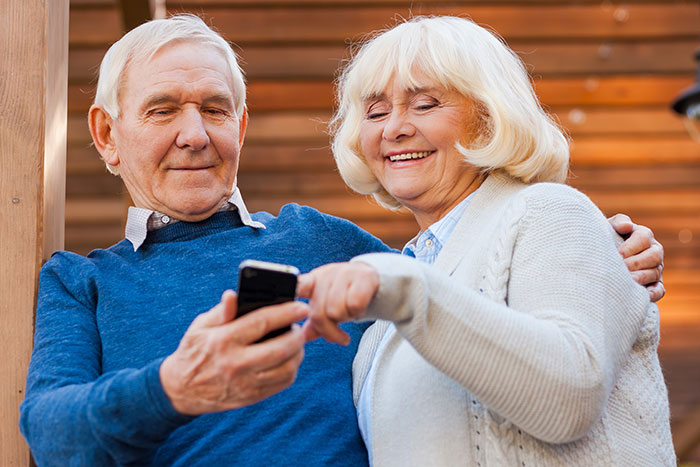 Pareja de edad avanzada sonriendo mientras usa un teléfono inteligente, simbolizando el seguimiento del teléfono y el intercambio de ubicaciones con los padres.
