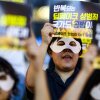 Esta foto muestra a los activistas con máscaras de ojos blancas y sosteniendo carteles leyendo (en coreano)