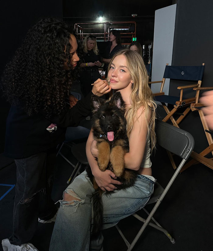 Sydney Sweeney sosteniendo a un cachorro detrás del escenario mientras se maquilla, en relación con la controversia de los cachorros de Gala Met.