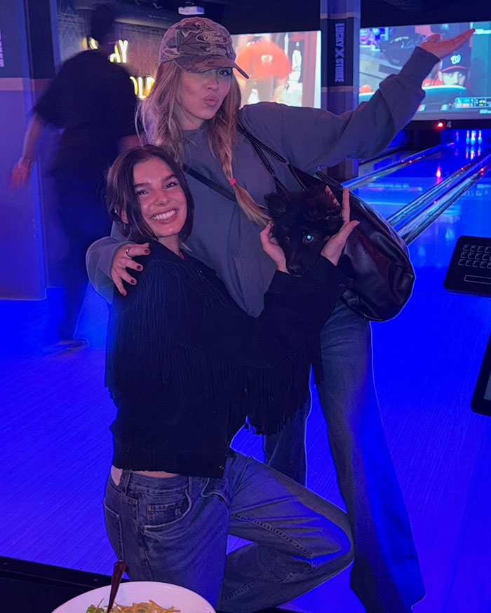 Dos mujeres posando con un pequeño cachorro negro en el interior, capturando un momento vinculado a Sydney Sweeney se estrenó por un cachorro desfilando.