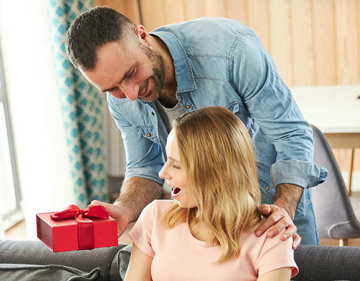 Hombre entregando un regalo a su sorprendida esposa embarazada a la que aún no considera a una madre para el Día de la Madre.