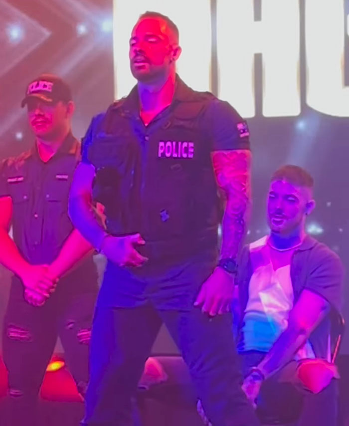 El hombre vestido como oficial de policía actuó en el escenario con otros, relacionado con la ex bailarina del pole con la historia de los buscadores de atención de los monjes.