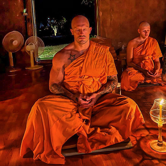Ex bailarina con túnicas de monje naranja, meditando en una habitación con poca luz con otro monje en el fondo.