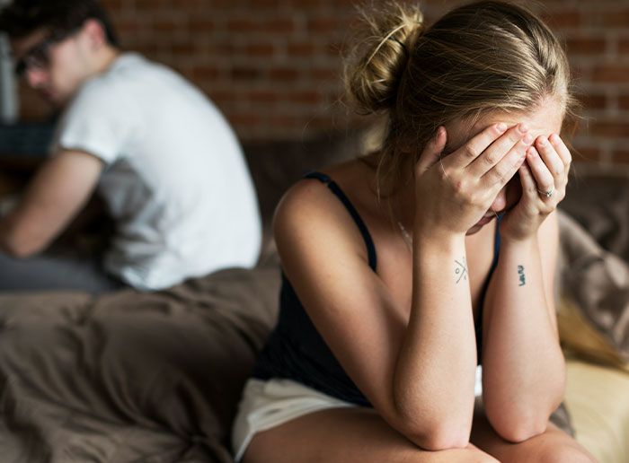 La mujer se sienta en la cama que cubre la cara en estado de shock, el esposo se da vuelta, capturando la reacción a la sorpresa de la prueba de embarazo.
