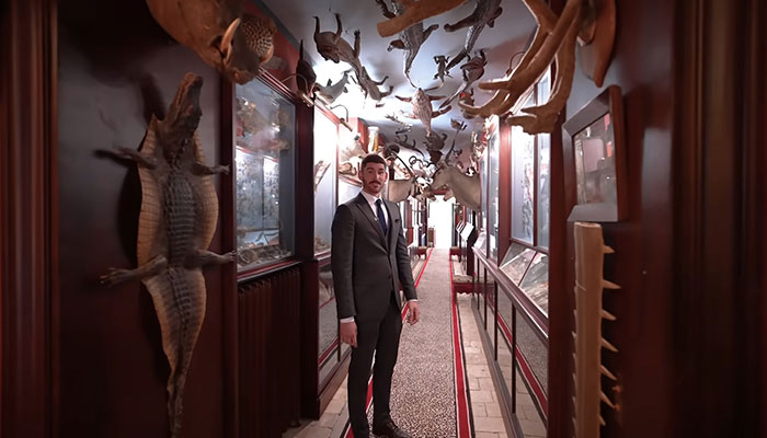 Hombre en un traje de pie en un pasillo de la casa más cara del mundo con decoraciones de animales montadas en las paredes y el techo