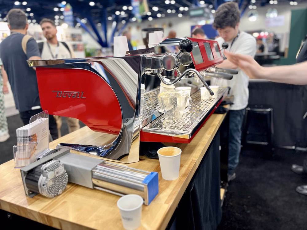 Un stand en SCA Expo 2025 muestra una máquina de café espresso roja de la marca Duvall.