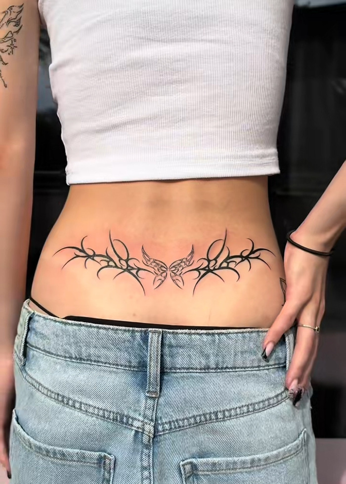 Tatuaje de la espalda baja con mariposa y diseño tribal, ilustrando la pluma del tatuaje y la visión experta de enfriarse en 2025.