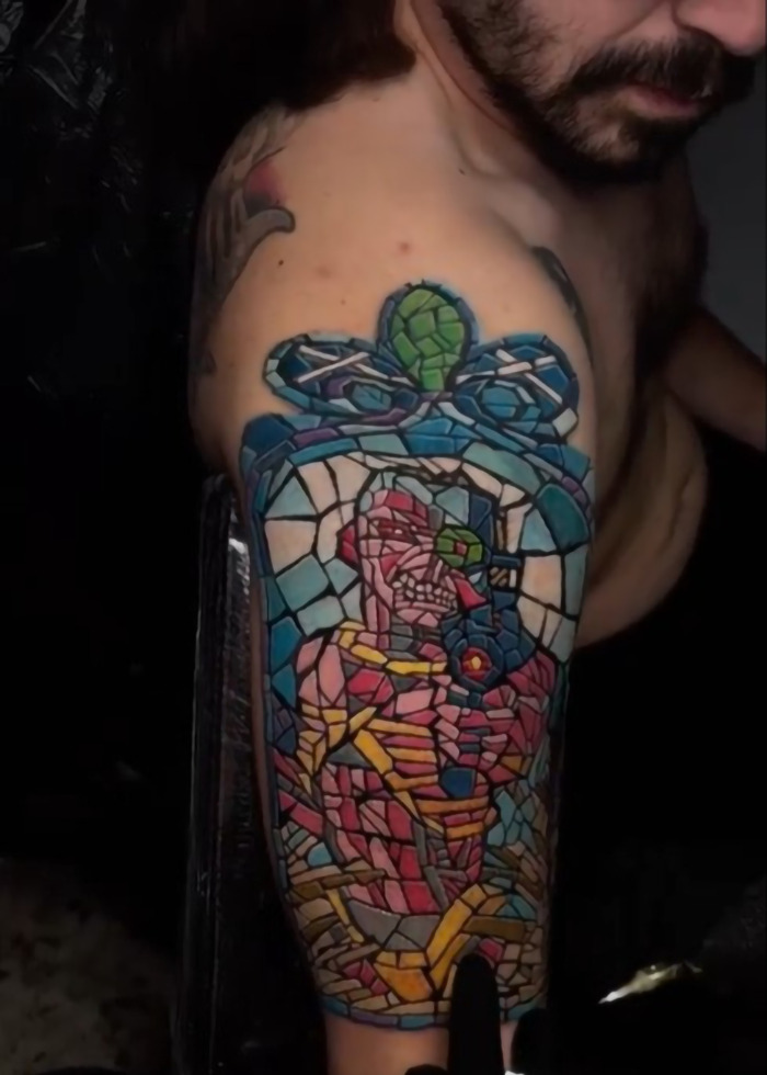 Hombre con colorido tatuaje de estilo mosaico que cubre la parte superior del brazo, resaltando la pluma del tatuaje que se enfría en 2025.