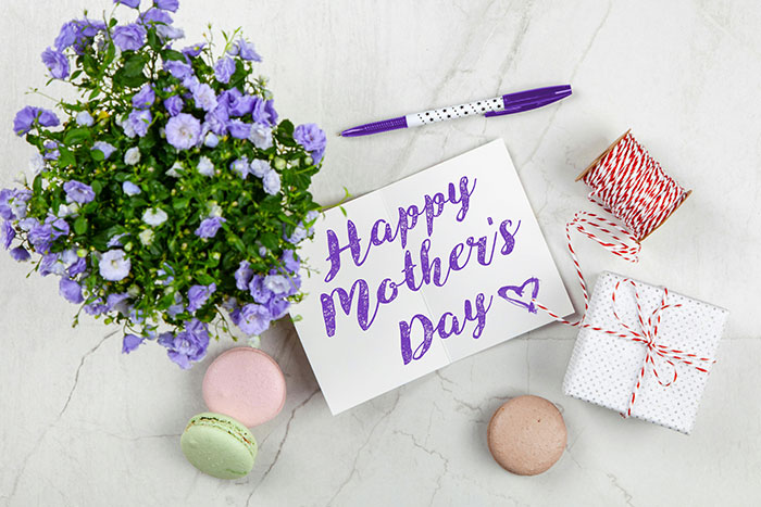 Tarjeta del Día de la Madre con flores, caja de regalo y macarons que simbolizan a la madre de perro que busca el mismo trato de MIL.