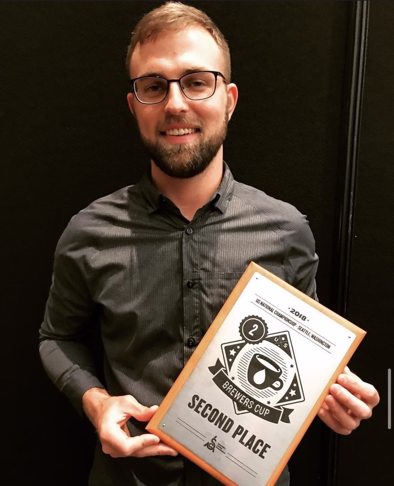 Justin Goodhart sonríe, sosteniendo una placa que lee el