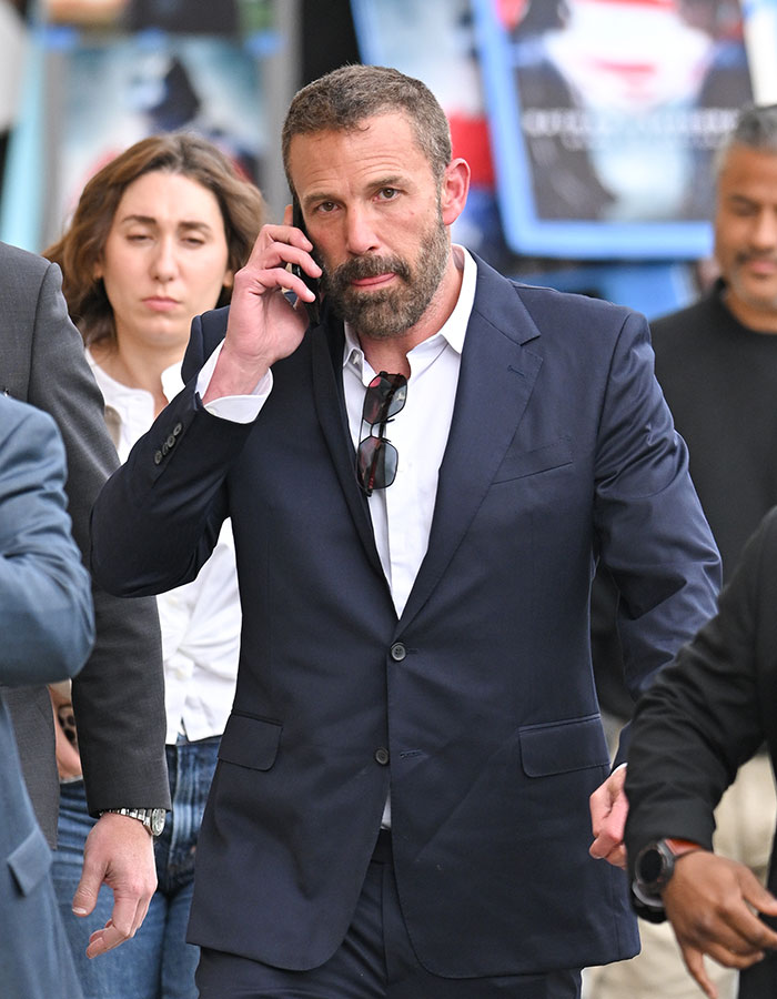 Hombre con un traje oscuro que habla por teléfono, rodeado de personas, relacionados con las noticias de mal funcionamiento del vestuario de la estrella de Netflix Star Viral.