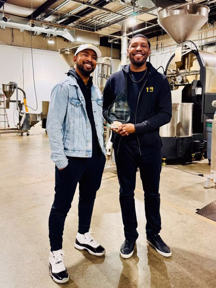 The Insider 03/09: Una foto de Pernell Cezar y Rod Johnson de BLK & Bold Specialty Beverages sonriendo sosteniendo un trofeo de vidrio, parte de la presentación de premios de CCRE.