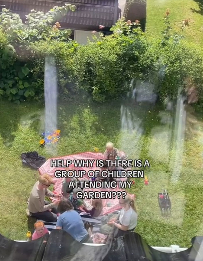 Grupo de extraños haciendo un picnic en el patio mientras la mujer mira, desconcertada y confundida por la inesperada reunión.