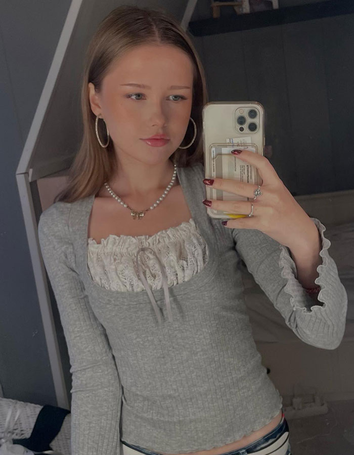 Mujer joven tomando una selfie, apareciendo desconcertada cuando extraños tienen un picnic en su patio en el fondo.