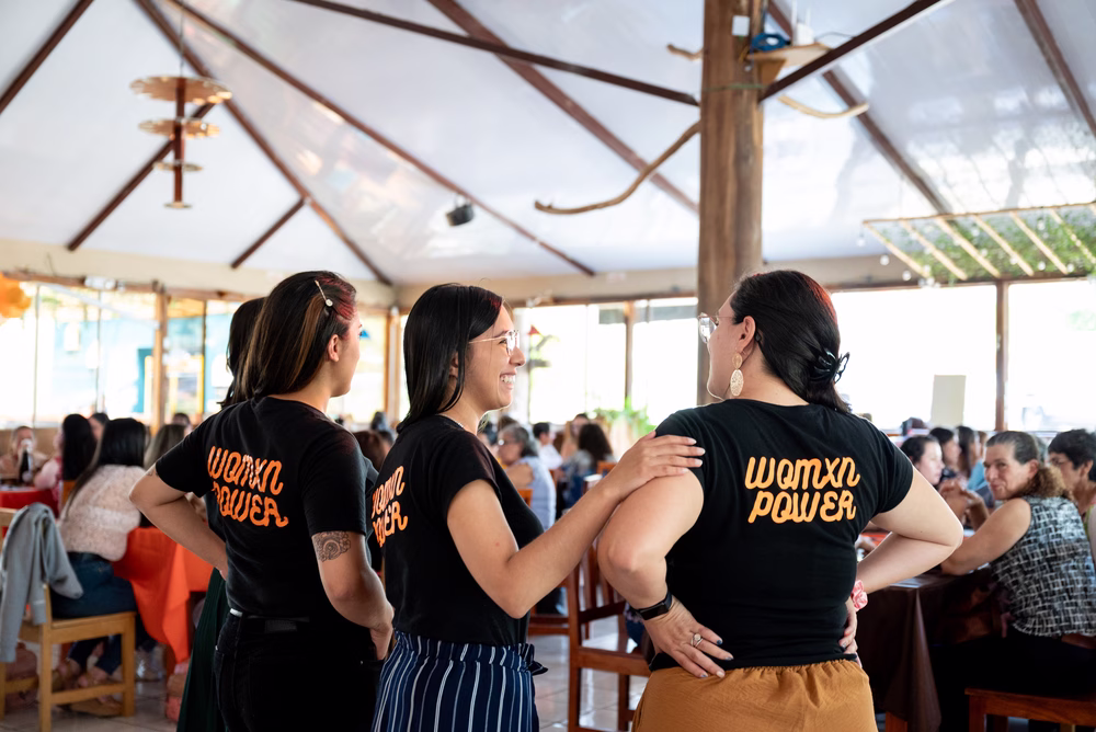 Un grupo de mujeres de pie, sonriendo, con camisas que decían