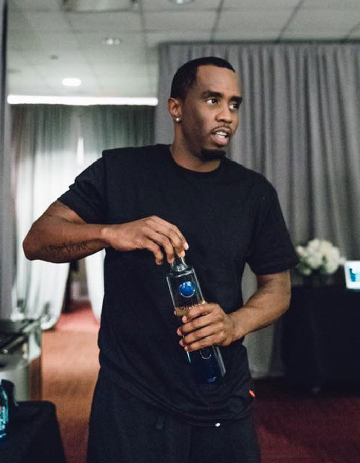 Diddy con una camisa negra sosteniendo una botella en el interior, destacando los informes de sus repugnantes hábitos alimenticios revelados por el antiguo personal.