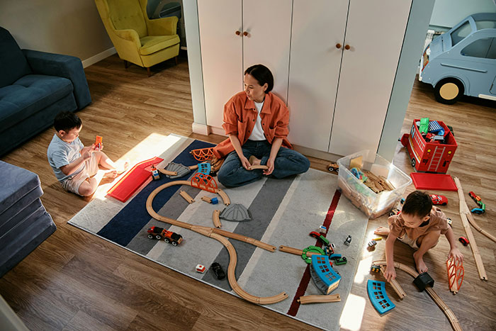 La niñera jugando con dos niños en el piso con tren de madera colocada mientras el bebé se queda dormido en el hogar familiar.