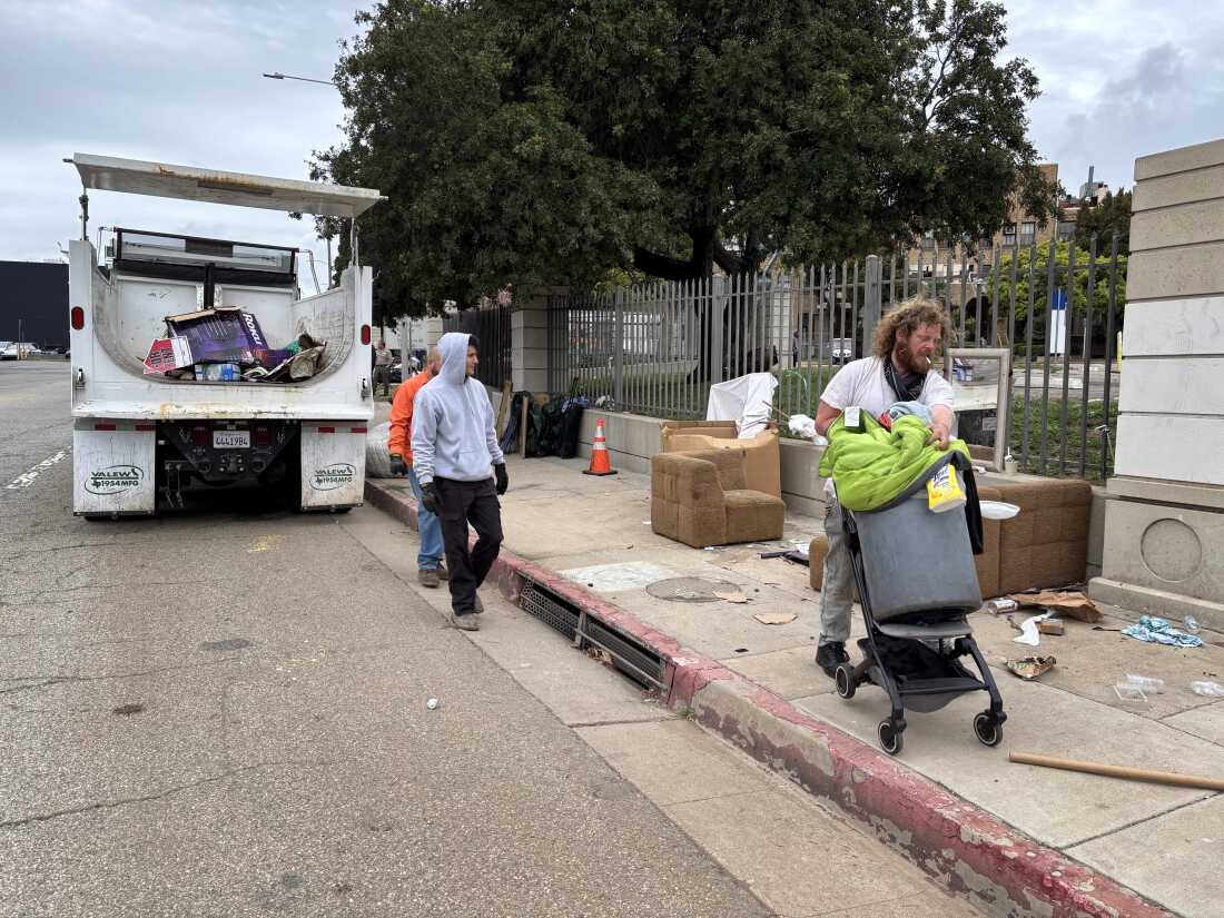 El veterano de la guerra de Iraq, Irving Webb, mueve sus pertenencias a medida que los trabajadores de saneamiento aclaran la acera, donde pasó algunas noches en abril, fuera del campus de Los Ángeles VA.