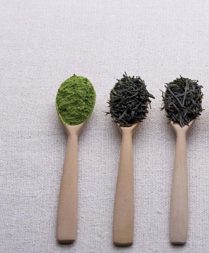 Tres cucharas de madera están llenas de matcha y hojas de té.