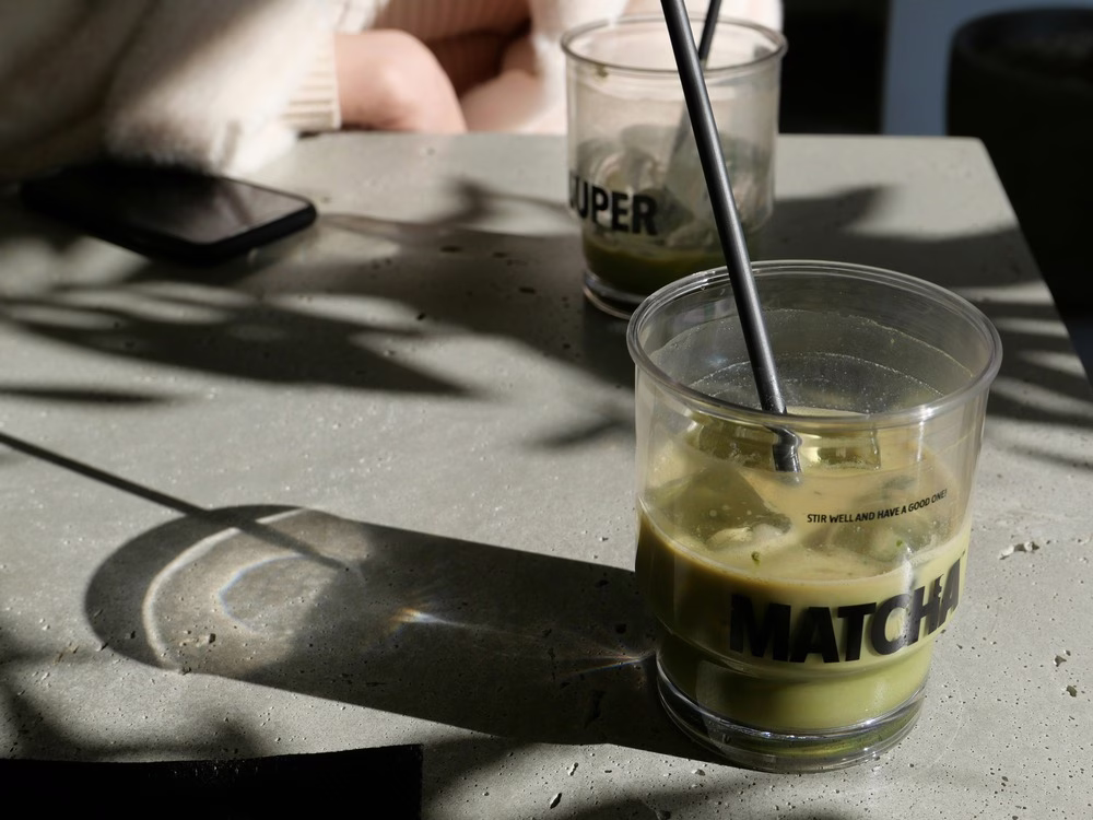 En una mesa de café hay dos bebidas de matcha helada medio llena.
