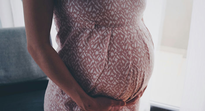 Mujer embarazada acuna su vientre en el interior, representando a un hijo adolescente quedando embarazada con el concepto de propósito.