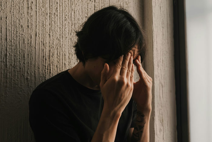 Hijo adolescente sentado en el interior con la cabeza en las manos, pareciendo estresado y preocupado por dejar embarazada a la novia a propósito.