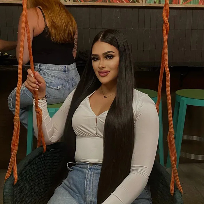 Mujer joven con cabello largo y oscuro sentado en un columpio en el interior, atuendo casual, sonriendo a la cámara.
