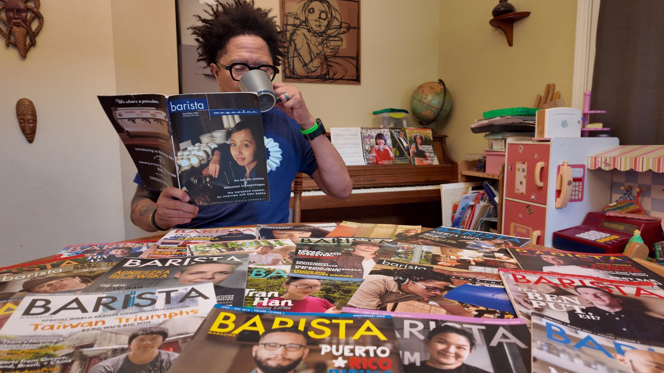Lem Butler leyendo la edición de abril + mayo de 2005 de la revista Barista mientras tomaba un café con docenas de otras revistas Barista en una mesa frente a él.