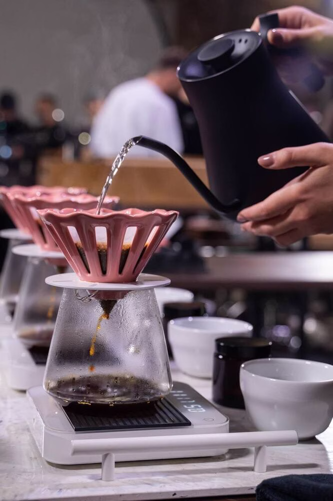 Un primer plano de alguien que vierte agua caliente en un cervecero de café rosa en forma de geométrica: el cervecero Dotyk de Ucrania.