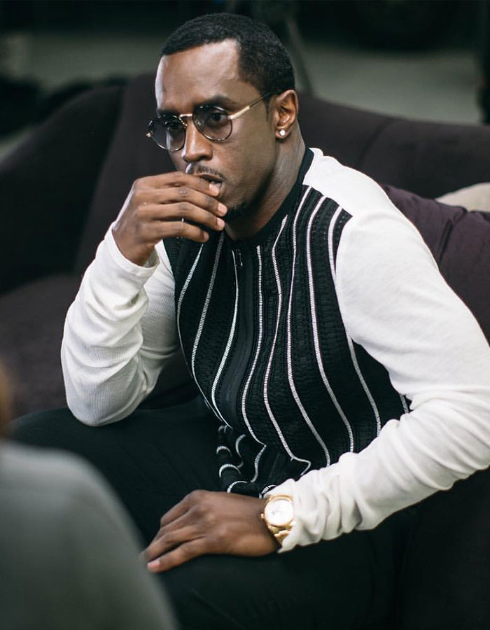 Hombre con gafas de sol y un suéter blanco y negro sentado cuidadosamente, relacionado con los repugnantes hábitos alimenticios de Diddy revelados por el personal.