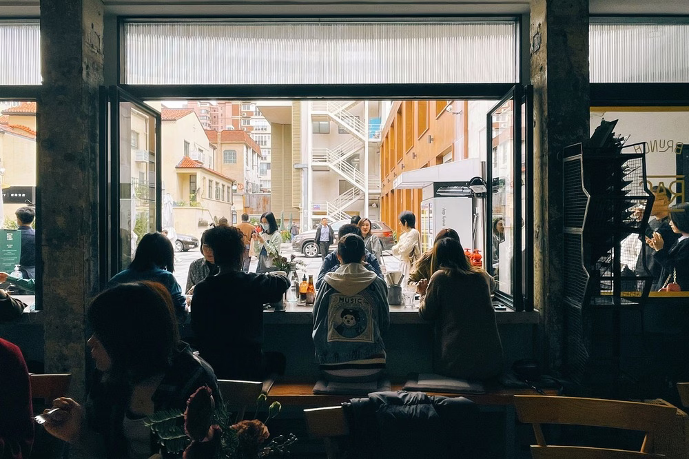 Una vista desde un café en Shanghai, China, muestra a un grupo de personas sentadas en un bar con una gran ventana que mira a una calle concurrida.