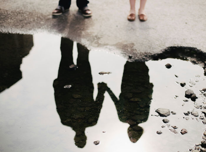 El reflejo de un hijo adolescente y una novia tomados de las manos cerca de un charco, simbolizando el hijo adolescente, quede embarazada a propósito.