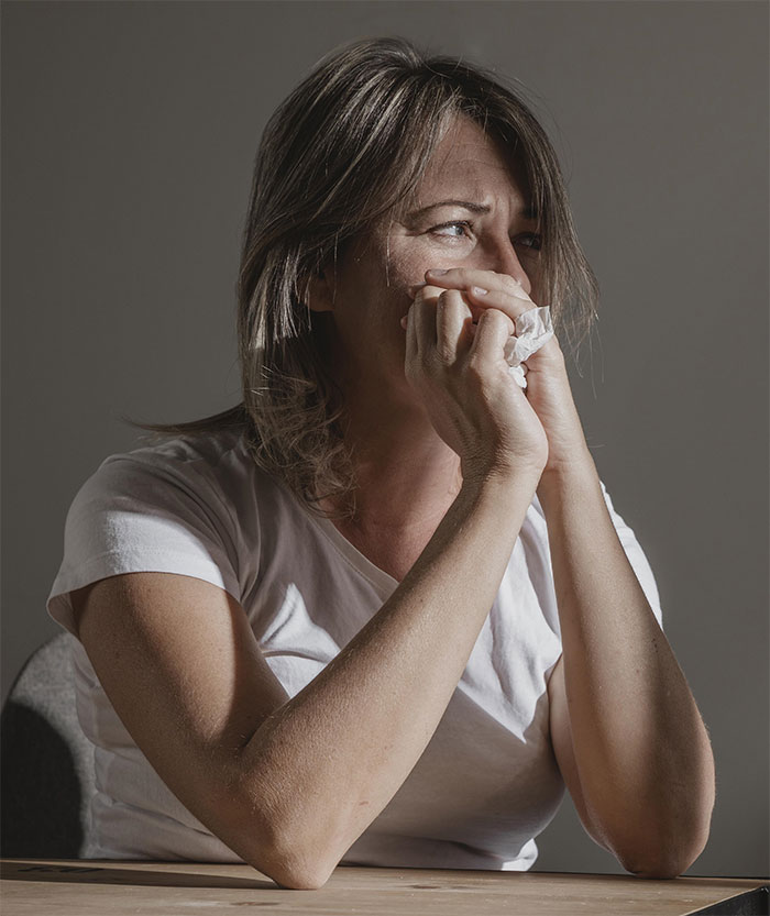 Mujer con cáncer que se ve angustiada mientras está sentada en una mesa, sosteniendo un pañuelo y reflexionando sobre las tareas y el apoyo.